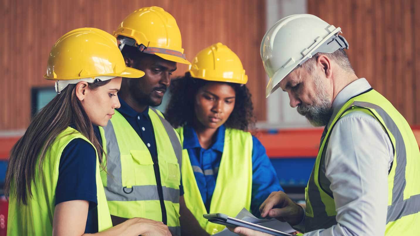three construction workers wearing yellow hard hats and reflective vets and site manager in a white hard hat