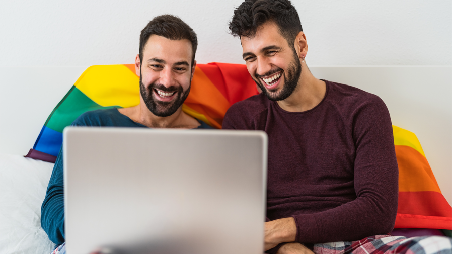 two-gay-men-smiling-looking-at-laptop-pride-flag