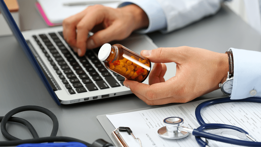 provider on laptop holding pill bottle and sending prescription to pharmacy for telehealth patient