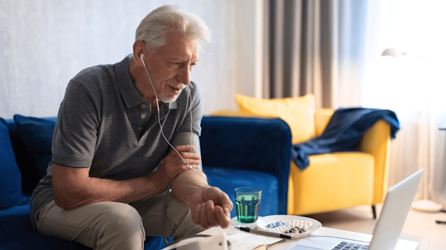 Older man sitting on the coach using an at-home blood pressure device