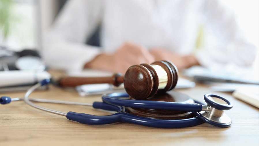 stethoscope wrapped around a gavel laying on a desk with blurred white male in the background