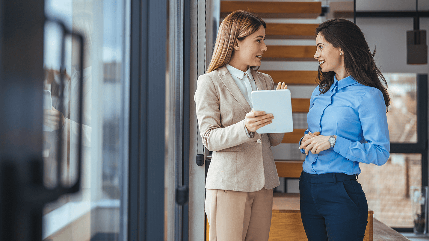 woman in tan suit talking to another woman in blue button up about employee benefits