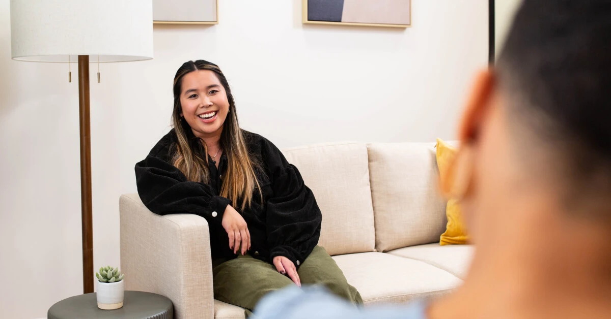 An asian woman smiles as she's in a talk therapy session with her Black female therapist.