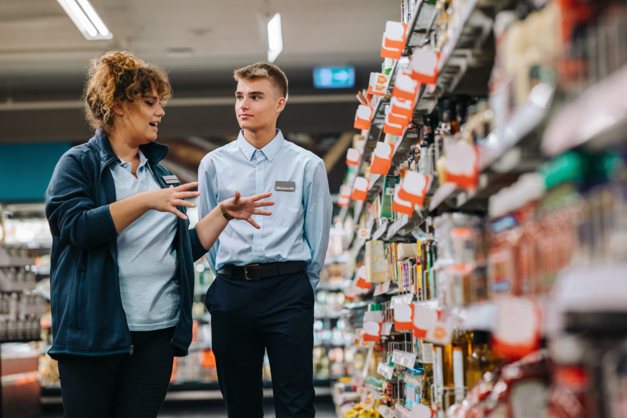 Supermarket manager training an employee while walking down a supermarket aisle.