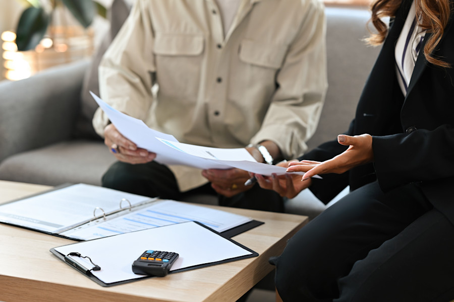 Two people sitting at a table, looking at and discussing some papers or documents. There is a calculator on the table implying they are discussing financial matters.