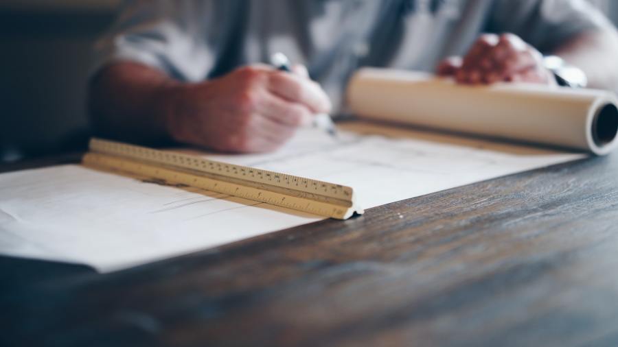 Architect sitting at desk drafting a design on blueprint paper. 