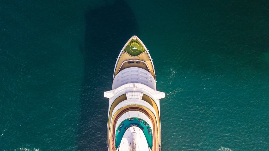 Cruise ship swimming through blue-green waters, pictured from above.