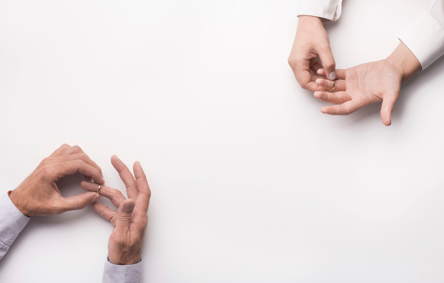 Man and woman each taking off their wedding ring. Only their hands are pictured and at opposite sides of the image.