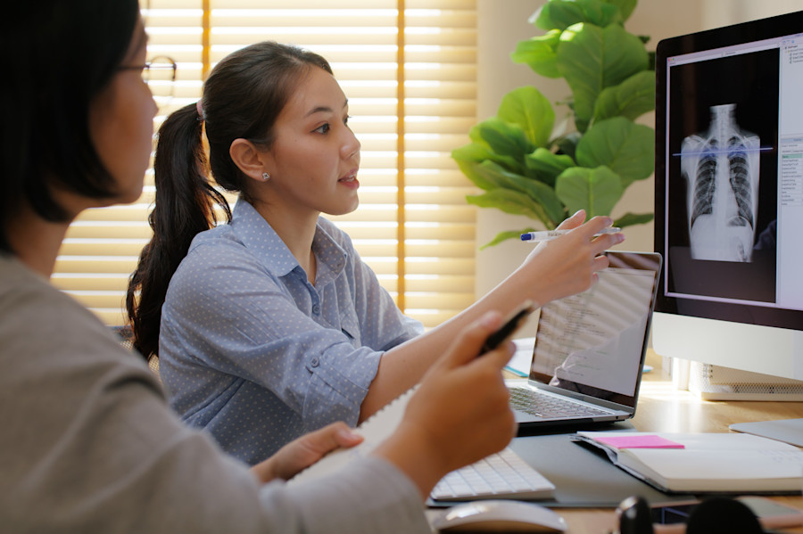 Two medical professionals sitting at a desk looking at and discussing an X-ray on a computer screen. 
