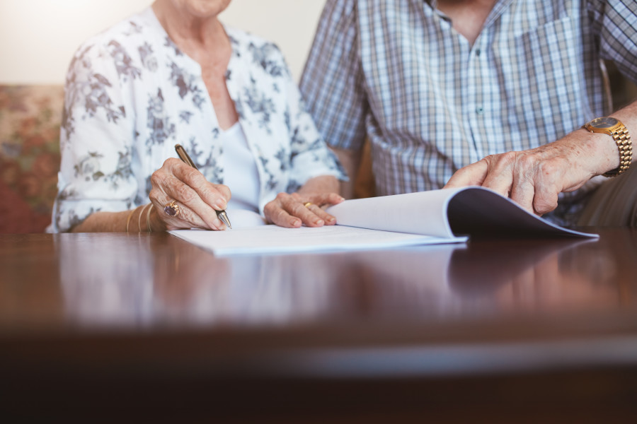An elderly couple reviewing and signing documents in a lawyer or financial advisor's office.