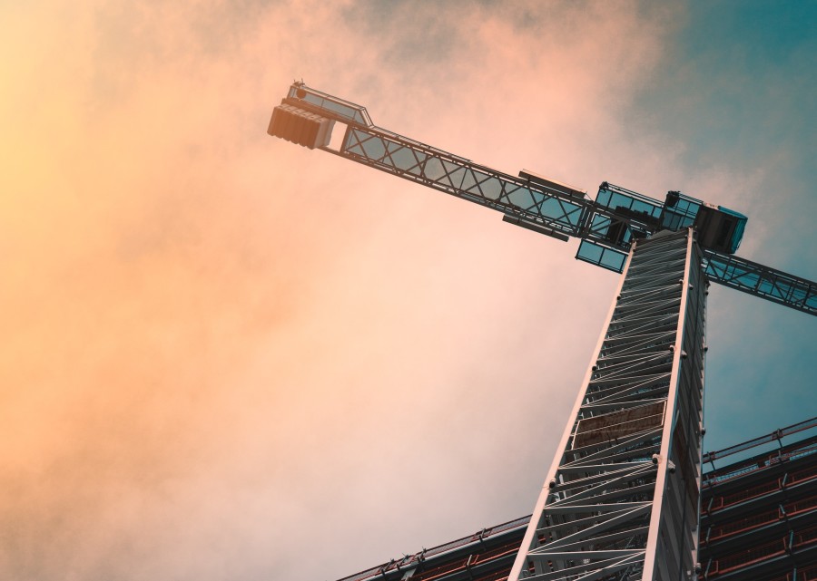 A construction crane, shot from a low angle, against a cloudy sunrise sky.