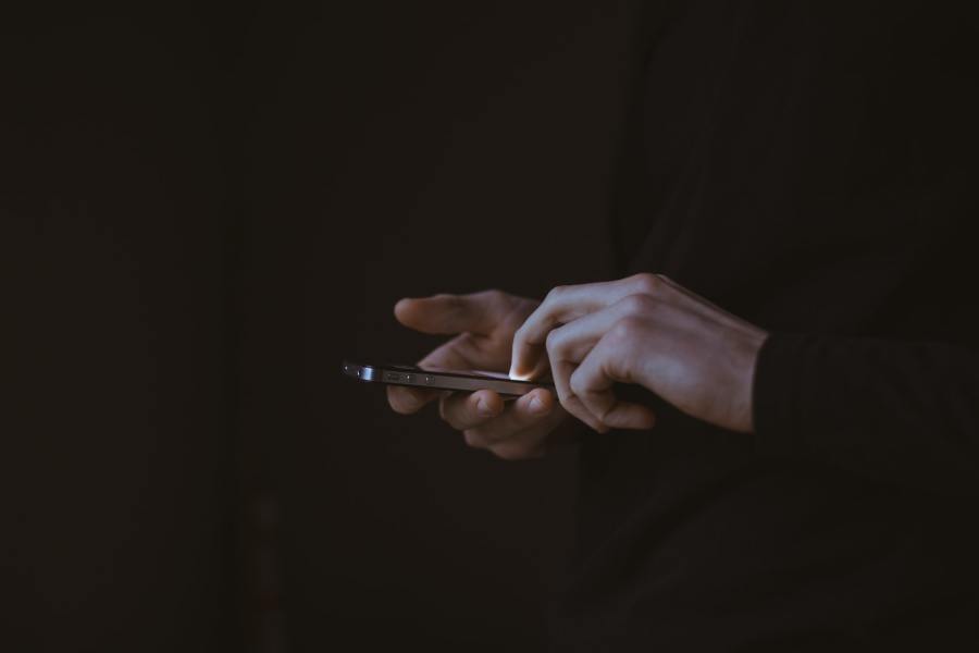 A pair of hands holding and using a mobile phone, set against a dark background.