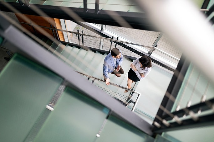 Image: Man and woman speaking in an office corridor.