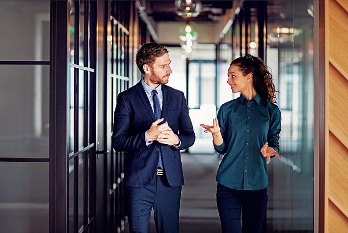 Two colleagues talking and walking down a hallway.