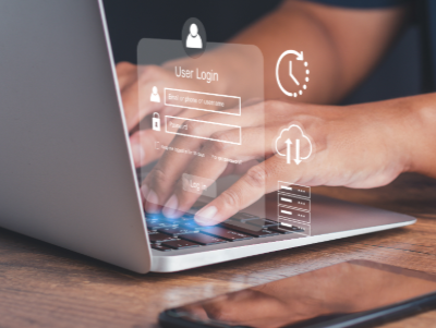 A close-up image of hands typing on a laptop keyboard with translucent digital interface icons floating above the screen. The overlay includes a user login form, cloud storage symbol, security padlock and data transfer icons, representing cybersecurity, digital access and cloud-based technology.