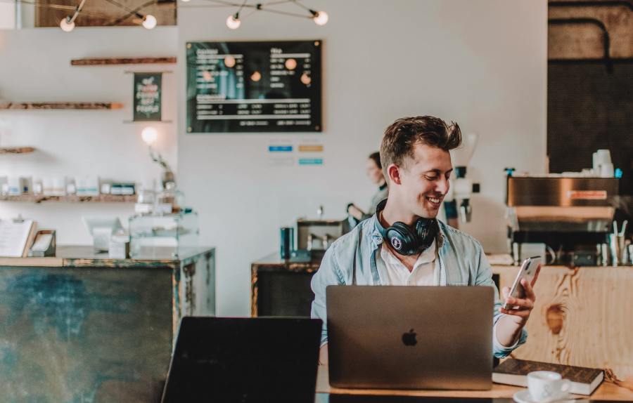 Young man in a cafe is looking at his mobile phone and smiling.