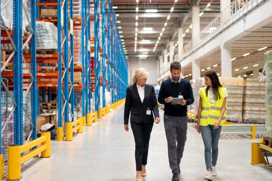 Three managers walking through a large logistics warehouse