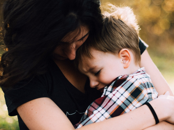 A mother hugging and protecting her upset child son.