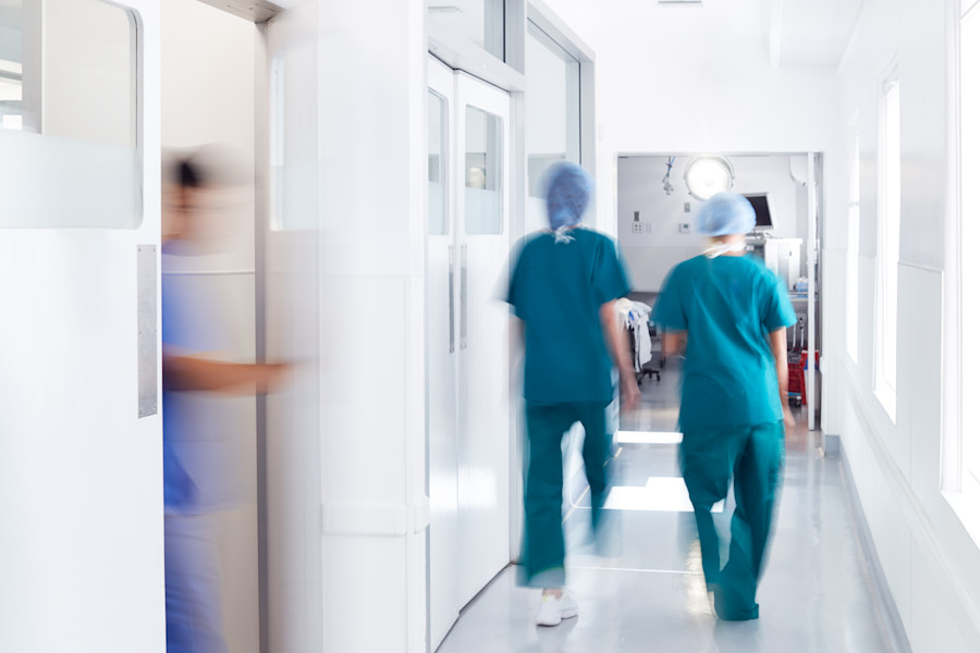 Doctors or medical professionals walking down a hospital corridor. They are wearing scrubs and surgical caps.
