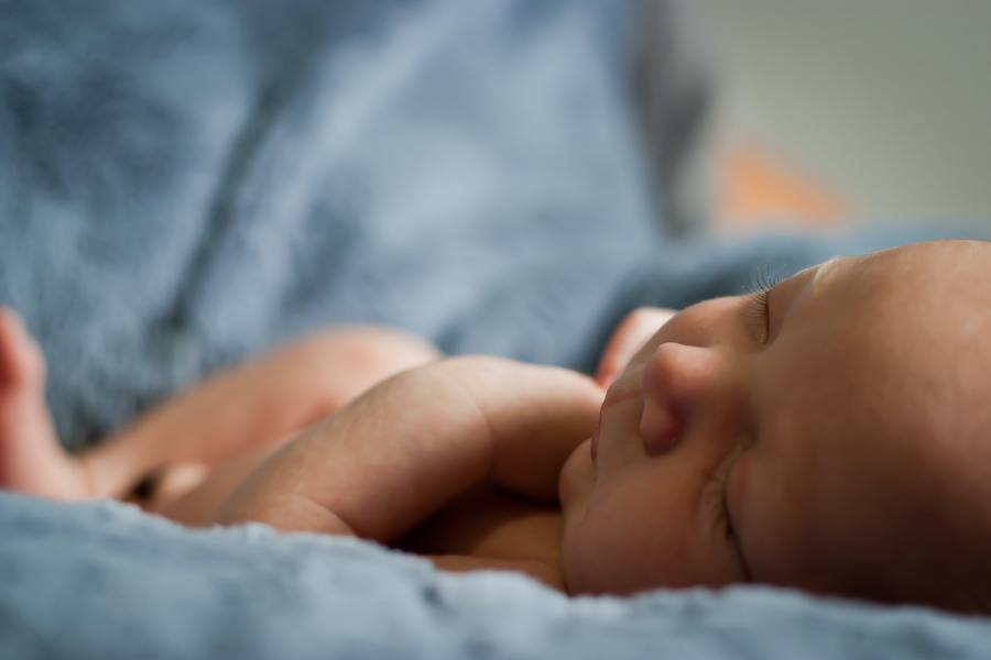 A close-up image of a one-week old baby sleeping on a blue blanket.