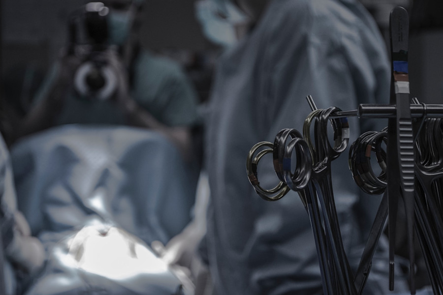 Surgical scene with surgical instruments in the foreground and surgeons undertaking a procedure in the background.