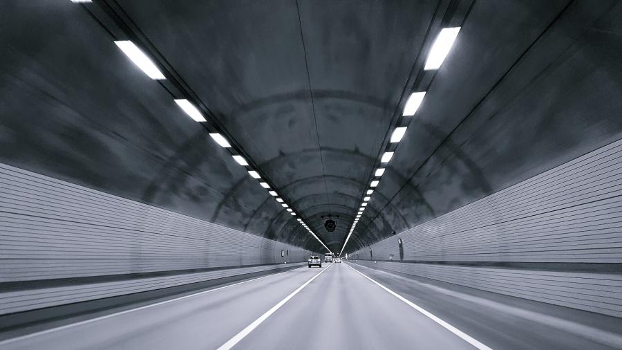 Grey and white photograph of a motor tunnel with cars driving down it.