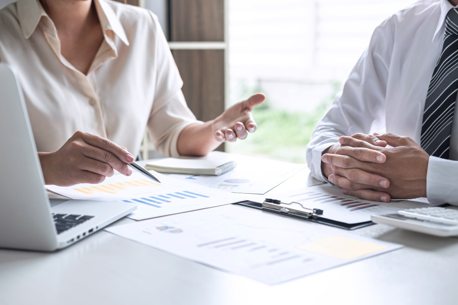 Man and woman in corporate dress sitting at a table and discussing business reporting or financial results.