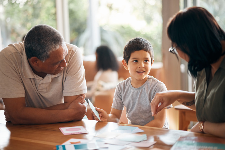 Child sitting at a table with parents or family members. He is playing with flashcards.