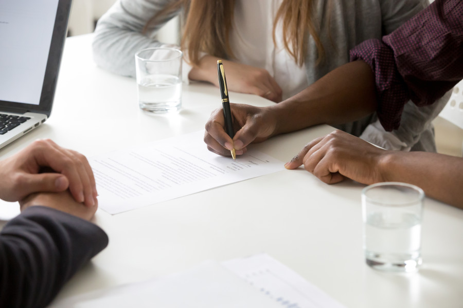 A man and woman sitting across the desk from a legal or financial advisor. They are signing documents.