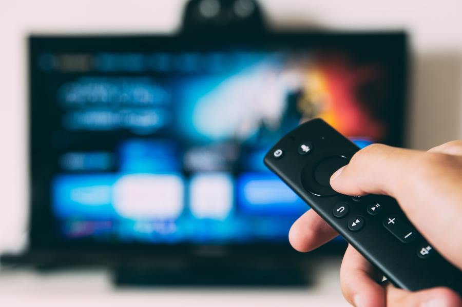 Person with remote control selects a film to watch on a streaming service on a television. 