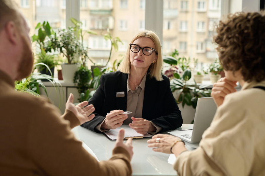 Man and woman sitting across the desk from a family lawyer or advisor. The man is speaking and gesticulating while the lawyer/advisor looks at him and listens.