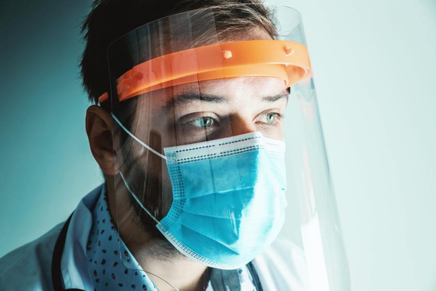 Doctor in face mask and face shield looks into the middle distance. 