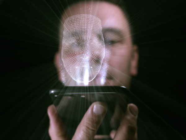 Close-up of a man's face as he looks into his mobile phone to activate facial recognition software. A digital image of a face scan is overlain on the image to represent the facial recognition software in action.