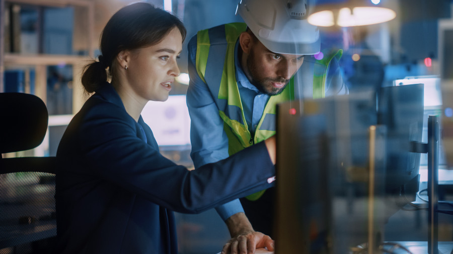 Female engineer working on a computer and showing a male construction worker or project manager a design solution on a computer screen.