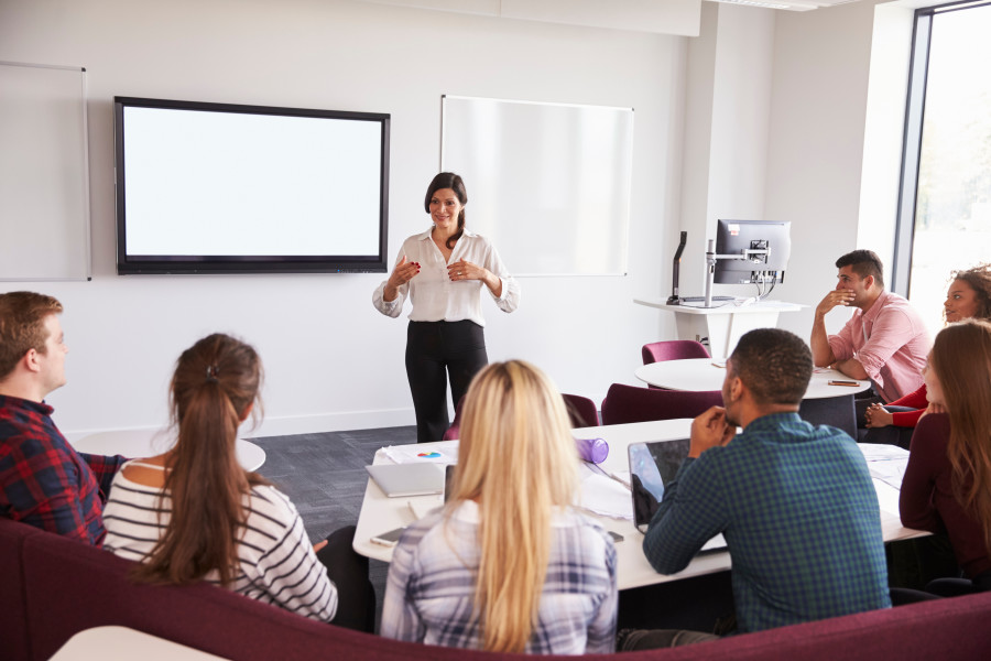 Female lecturer or tutor presenting to a university class in front of a whiteboard. 