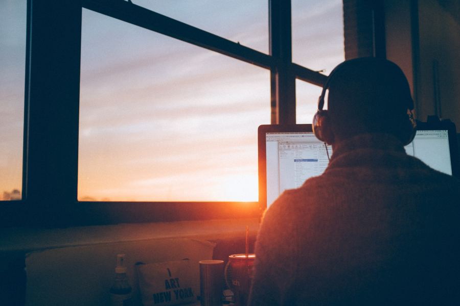 Man working on laptop in home office at sunset or sunrise.