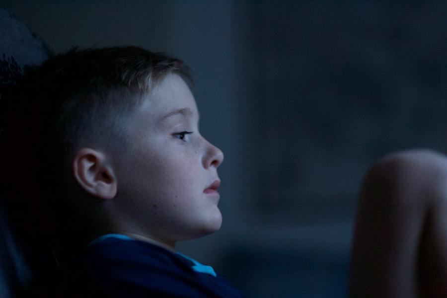Close-up in dim light of young boy looking pensively into middle distance.