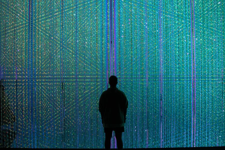 The silhouette of a man standing in front of a background of many small green and blue coloured lights.