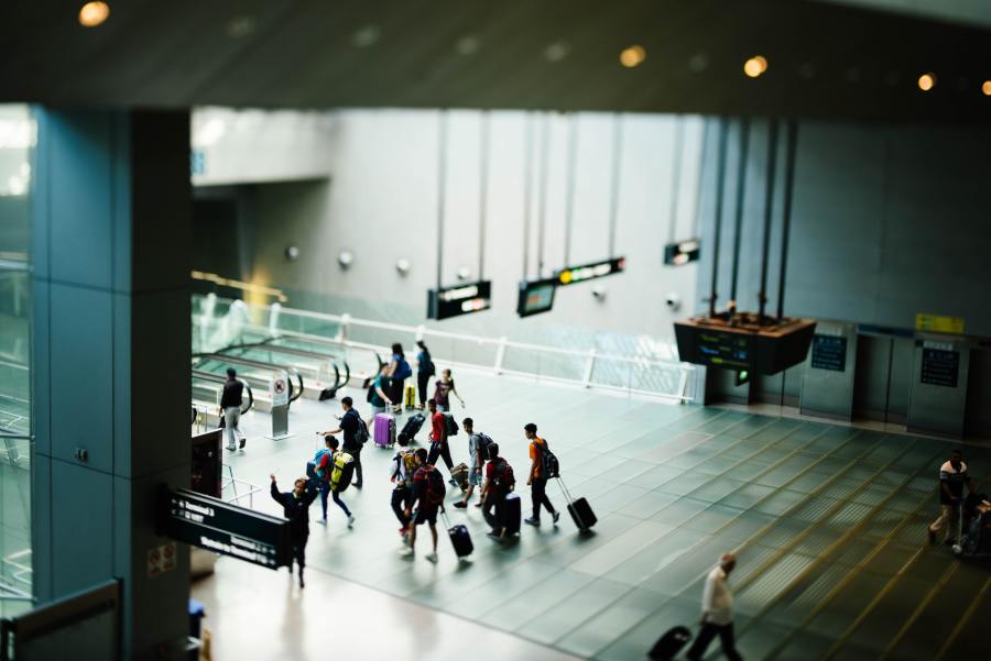 Long shot of the interior of an airport terminal. A number of people with suitcases are traversing the space.