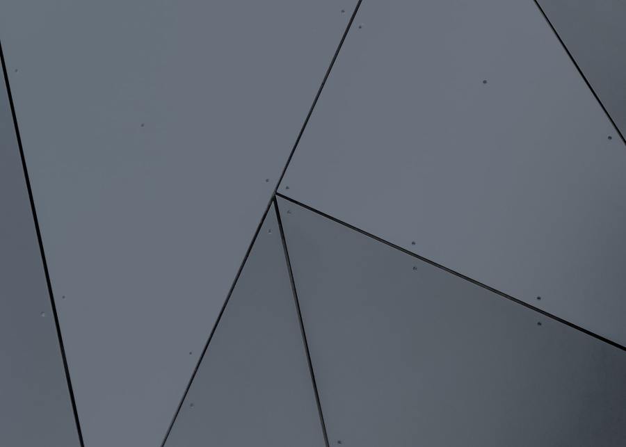 A close-up of grey exterior wall cladding in a geometrical triangular pattern.