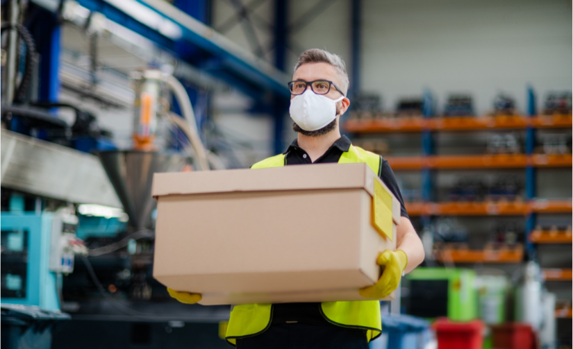 Worker in a warehouse carrying a box and wearing a protective face mask.