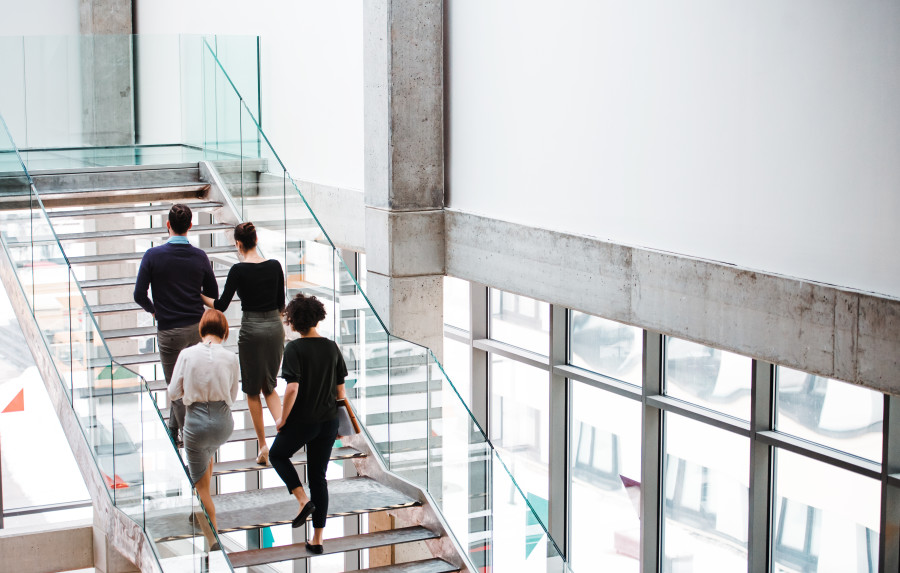 Group of four colleagues or employees ascending a staircase in a contemporary building or office space.