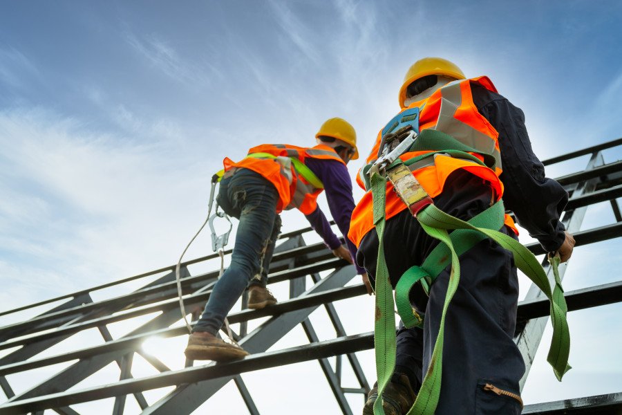 Two workers on a scaffolding structure wearing harnesses for safety.