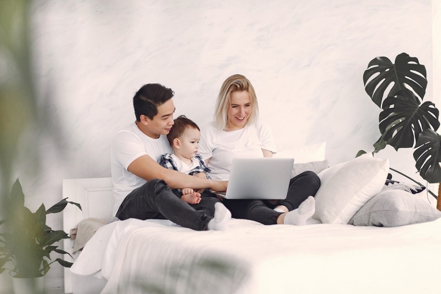A family sitting on a bed looking at a laptop. 