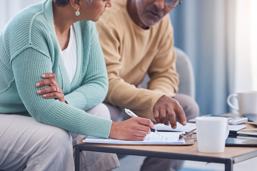 A man and woman sitting at a coffee table discussing and signing documents.