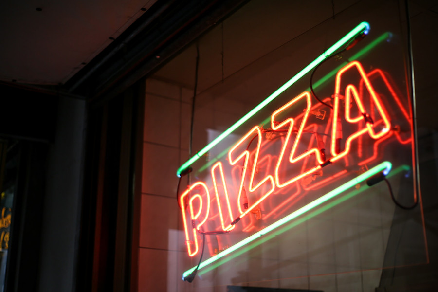 A neon sign in a restaurant window spelling the word 'pizza'.