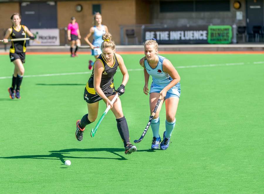 Women playing hockey on green pitch.