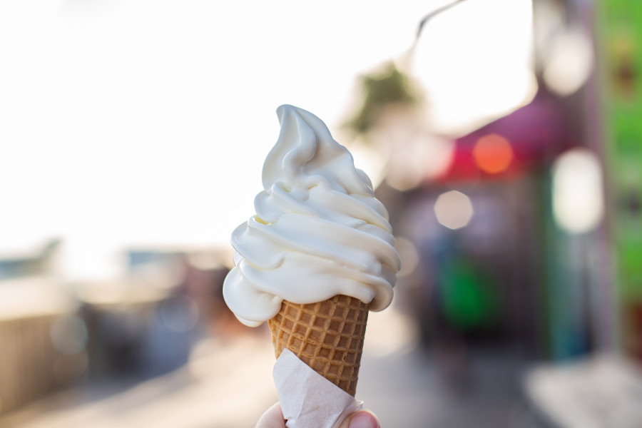 A vanilla soft serve ice cream cone set against a blurred coloured background.