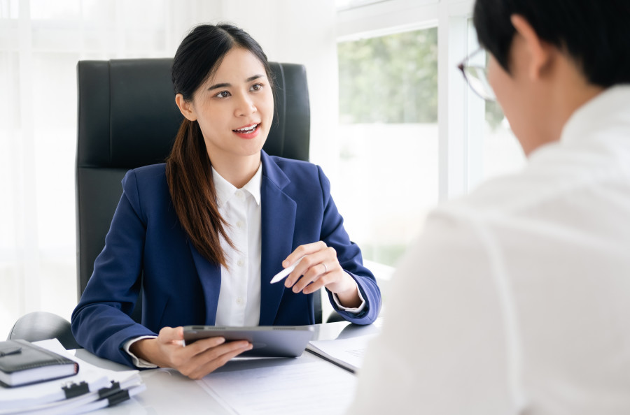 Female lawyer sitting at a desk speaking to a colleague or client while holding a digital tablet or iPad.