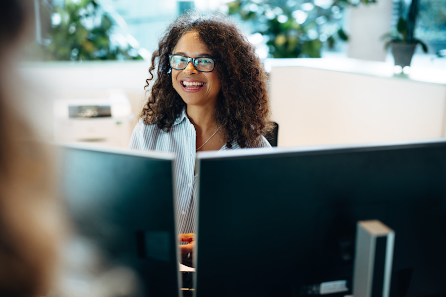 Government worker sitting behind two computer screens at a reception desk or in an office.